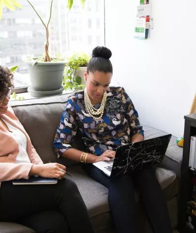 Twee vrouwen zijn samen in gesprek op de bank. Eentje heeft een laptop.