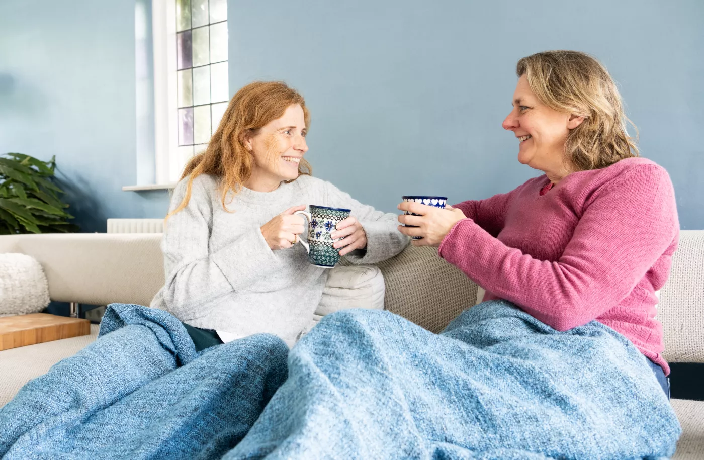 Twee mensen op de bank. Drinken een kop thee en zitten onder een deken.