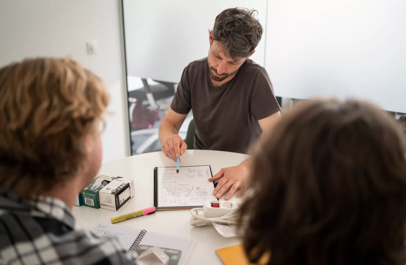 Drie personen zitten aan een tafel. Een van deze personen geeft energie advies aan de twee andere personen.