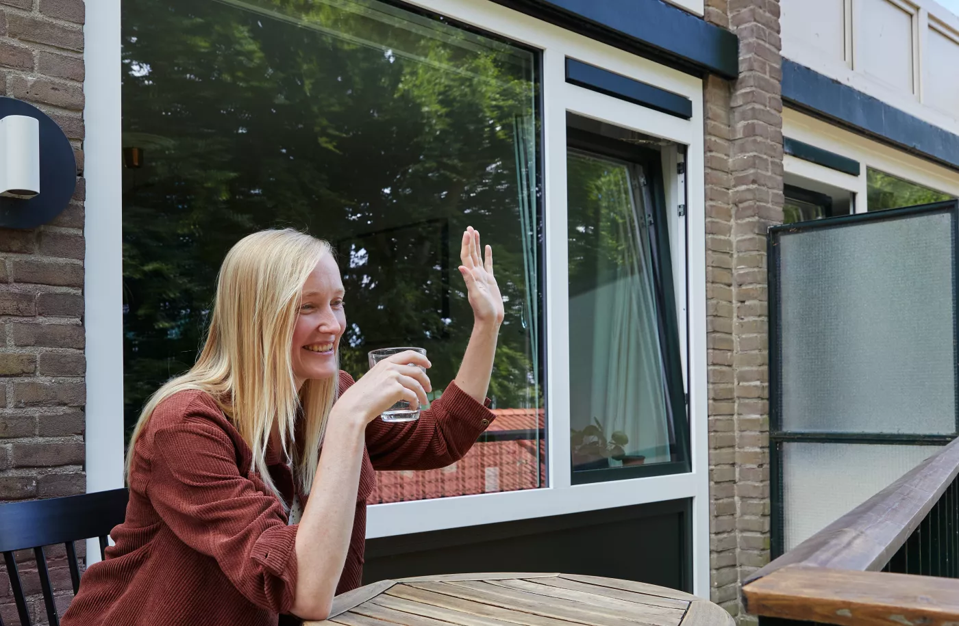 Inwoner zit op haar balkon en zwaait