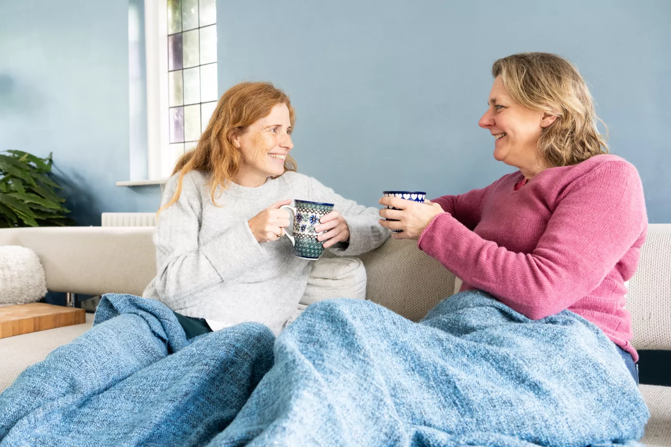 Twee mensen op de bank. Drinken een kop thee en zitten onder een deken.