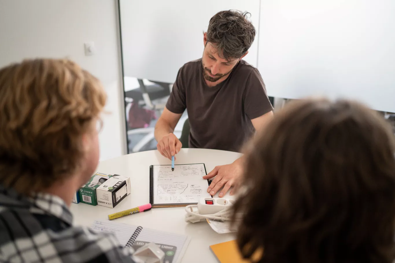 Drie personen zitten aan een tafel. Een van deze personen geeft energie advies aan de twee andere personen.